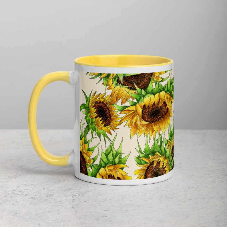 Puede incluir: Taza de cer&aacute;mica blanca con borde amarillo y un patr&oacute;n de girasoles sobre un fondo crema.