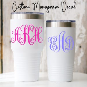 May include: Two white insulated tumblers with silver rims. One tumbler features a pink monogram, the other a blue monogram. The text "Custom Monogram Decal" is written in black script above the tumblers.