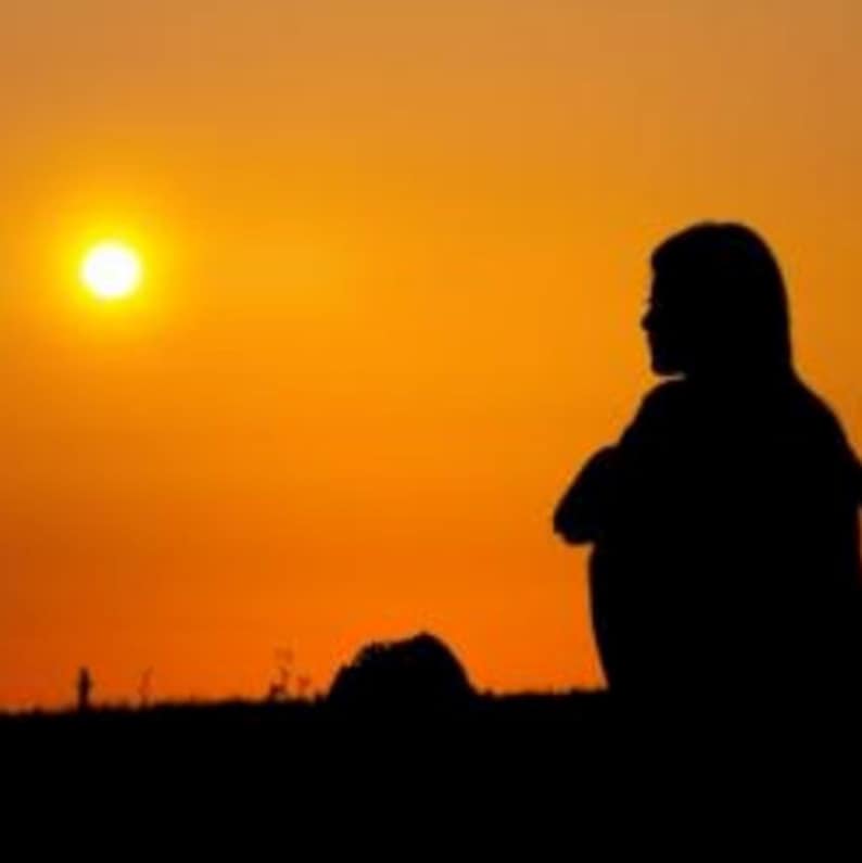 May include: Silhouette of a person sitting with their arms crossed, looking out at a bright orange sunset. The sun is a bright yellow circle in the sky.