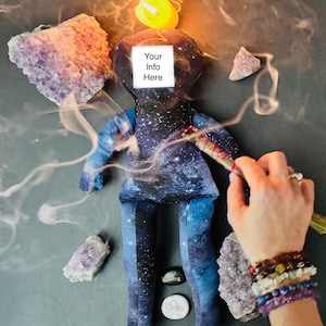 May include: A celestial-themed doll with a galaxy print, surrounded by amethyst crystals, a burning candle, and a smudge stick. The doll has a white square with the text "Your Info Here". Small stones with the words "Healing" and "Clarity" are also present.