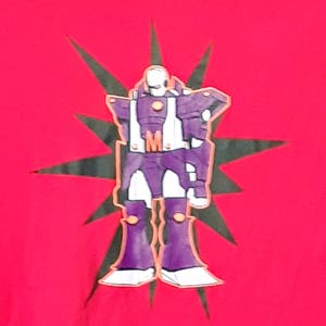 Pu&ograve; includere: Maglietta rossa con un disegno di robot viola, dettagli bianchi e arancioni e una stella nera. Il robot ha la lettera "M" sul petto. Il disegno &egrave; centrato.