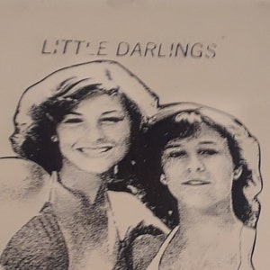 Könnte beinhalten: Schwarz-Weiß-Illustration mit zwei jungen Frauen, mit dem Text "LITTLE DARLINGS" über ihren Köpfen. Der Text "TATUM with KRISTY AGE 16 THE AWKWARD YEARS" ist unter der Illustration abgedruckt.
