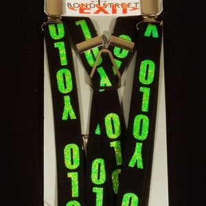 May include: Black suspenders featuring a bright green glittery "0101" pattern. The suspenders have silver-coloured metal clips and a Y-back design. The product is displayed on a white cardboard backing with the text "WAY OUT BOND STREET EXIT".