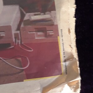 May include: A torn page with the text "Blonde on blonde by A. Tannenbaum" is visible. The image shows a red floor and a white table with a red chair.