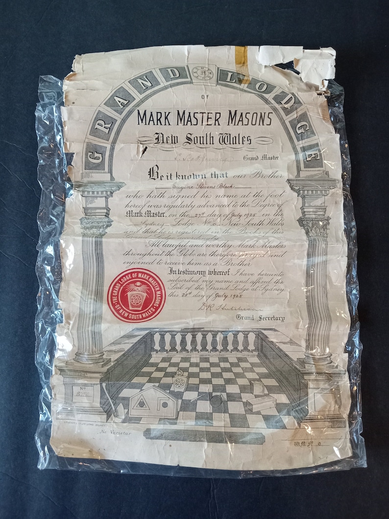 Puede incluir: Un documento antiguo de la Gran Logia de Maestros Masones de Marca de Nueva Gales del Sur, Australia, dentro de pl&aacute;stico. El documento presenta texto e ilustraciones ornamentadas, incluyendo un dise&ntilde;o de suelo a cuadros y un sello rojo.