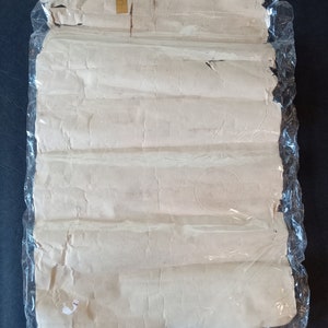 Puede incluir: Un paquete de papel enrollado, sellado en pl&aacute;stico transparente. El papel es blanquecino con pliegues visibles y un sello circular. El envoltorio de pl&aacute;stico est&aacute; ligeramente rasgado. Fondo azul oscuro.
