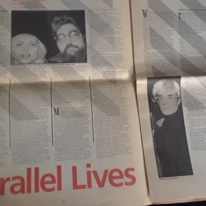May include: A newspaper spread featuring articles and photographs. The headline "Parallel Lives" is in red. Photos include two people and a portrait of Andy Warhol. The text is in black.