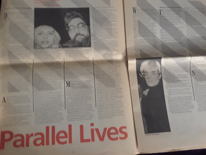 May include: A newspaper spread featuring articles and photographs. The headline "Parallel Lives" is in red. Photos include two people and a portrait of Andy Warhol. The text is in black.