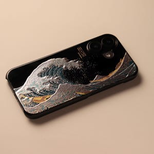 May include: Black phone case with an embossed wave design in silver, blue, and gold. The case has a glossy finish and a modern design. The phone case is a protective accessory for a mobile phone.