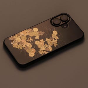 May include: A black phone case with a gold floral design. The case has a raised camera bump with two lenses.