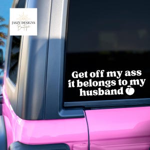 May include: A white vinyl decal applied to a vehicle window featuring the text "Get off my ass it belongs to my husband" followed by a small peach icon. The decal is displayed on the rear window of a bright pink vehicle with black trim.