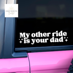 May include: A white vinyl decal applied to a dark car window featuring the text My other ride is your dad in a bold, rounded font. The text is flanked by small four-pointed star icons on both sides, creating a high-contrast graphic display.