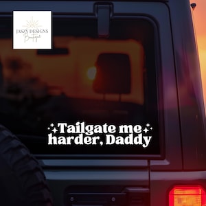 May include: A white vinyl decal applied to a vehicle window featuring the text Tailgate me harder, Daddy in a bold, rounded font, flanked by four-pointed star icons on both sides of the first line of text, creating a high-contrast graphic.