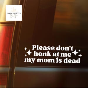 May include: A white vinyl decal applied to a vehicle window featuring the text "Please don't honk at me my mom is dead" in a bold, rounded font, flanked by four-pointed star icons on the left and right sides of the message.