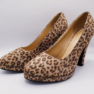 May include: A pair of platform pumps with a leopard print pattern. The shoes have a rounded toe, a thick platform sole, and a high heel. The print features brown spots on a tan background.