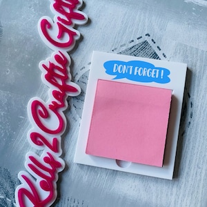 May include: White acrylic note holder with a pink sticky note and a blue speech bubble that says "DON'T FORGET!" The note holder is next to a pink acrylic sign that says "Kelly's Crafty Gifts".