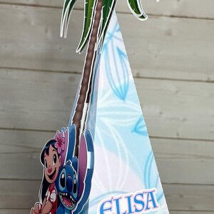 Op de afbeelding: Blauwe en witte feestversiering in de vorm van een kegel, met een palmboom en stripfiguren. De decoratie heeft de naam "Elisa" en het nummer "5" erop.