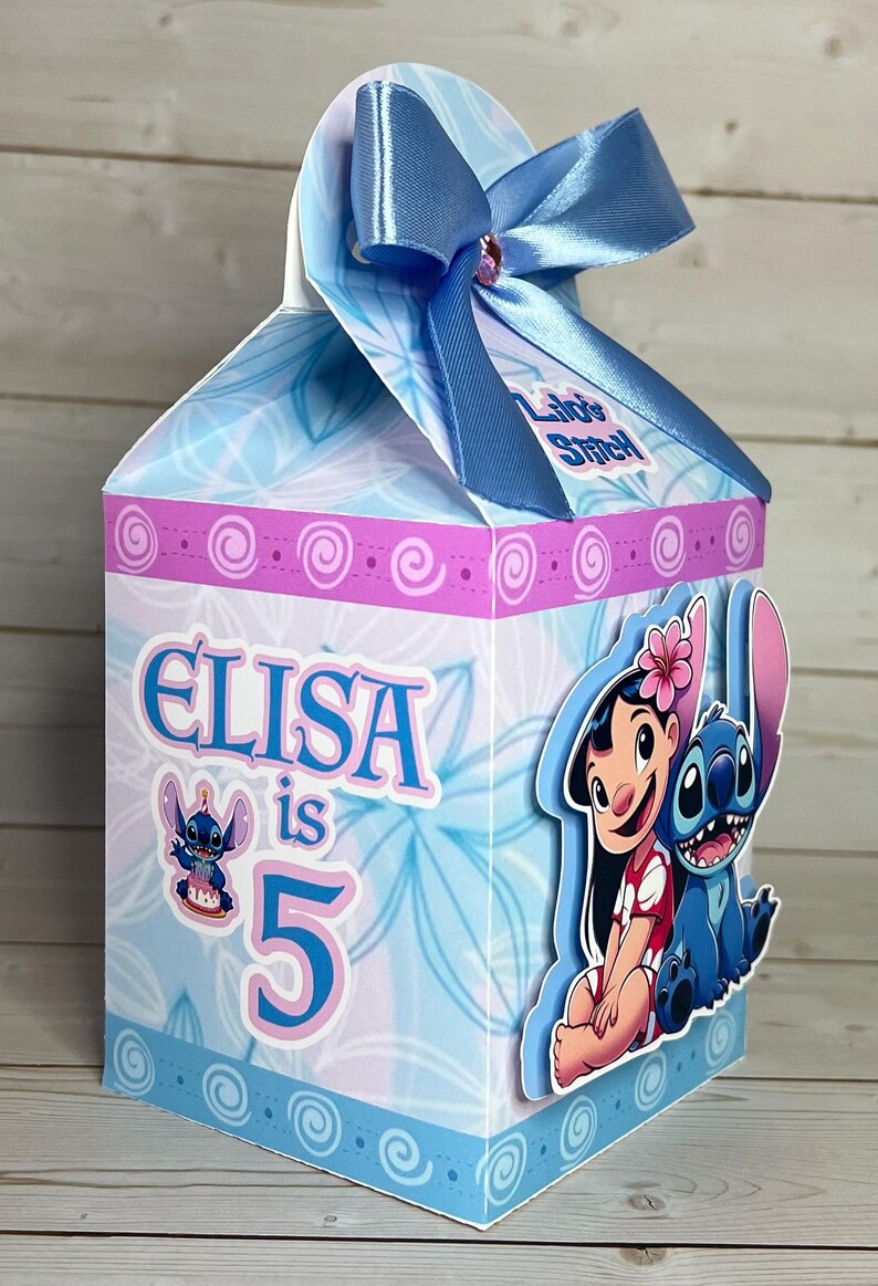 Op de afbeelding: Een lichtblauwe geschenkdoos met een bloemenpatroon en de tekst "Elisa is 5". De doos is versierd met afbeeldingen van Lilo en Stitch en een blauwe strik. Perfect voor een verjaardag.