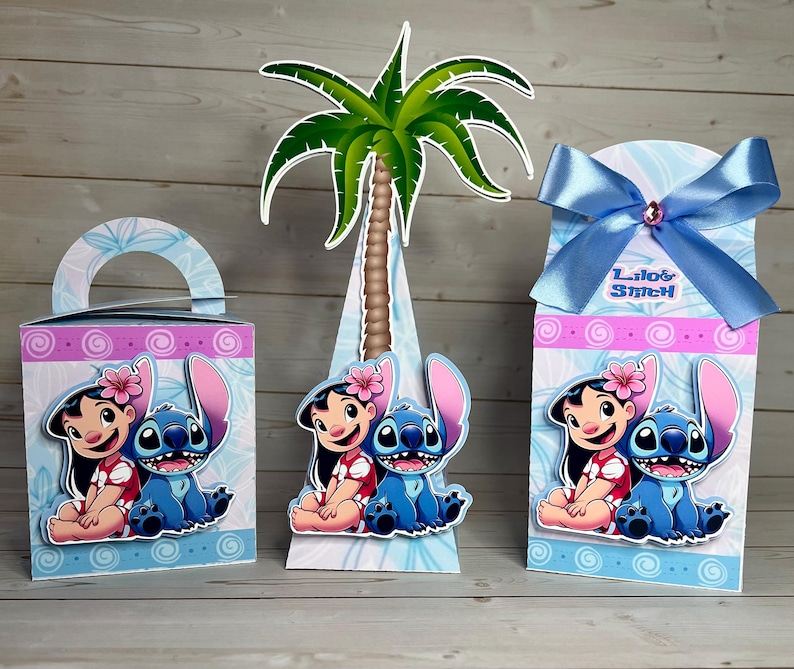 Op de afbeelding: Drie decoratieve dozen met de personages Lilo en Stitch. De dozen zijn blauw, roze en wit met een palmboom uitsparing. E&eacute;n doos heeft een handvat, een andere is kegelvormig en de derde heeft een blauw lint met de tekst "Lilo & Stitch".