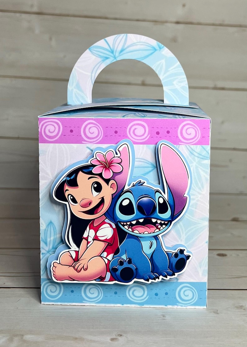 Op de afbeelding: Decoratieve geschenkdoos met de personages Lilo en Stitch. De doos heeft een lichtblauw handvat en is versierd met bloemmotieven en een roze en blauwe rand. Lilo draagt een rode jurk en Stitch is blauw.