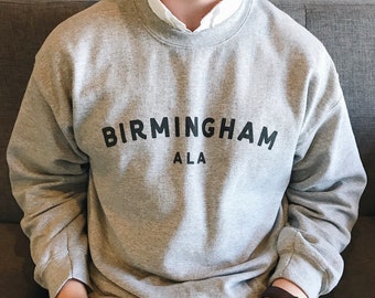 以下が含まれることがあります： 黒い文字で「BIRMINGHAM ALA」とプリントされたグレーのスウェットシャツです。