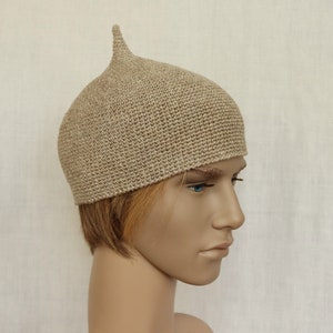 May include: A beige knitted hat with a pointed top. The hat is made of a soft, textured yarn.