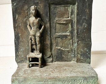 May include: A bronze sculpture of a person standing on a chair in front of a closed door. The sculpture is set against a textured background. The artist's signature, "S. PENJUS", is visible at the bottom of the sculpture.
