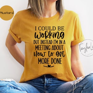 May include: A mustard yellow t-shirt with black text that reads "I could be working but instead I'm in a meeting about how to get more done".