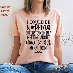 May include: A pink t-shirt with the text "I could be working but instead I'm in a meeting about how to get more done" printed in black.