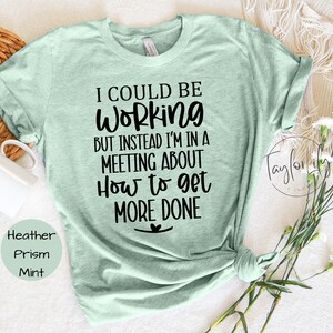 May include: A light green t-shirt with the text "I could be working but instead I'm in a meeting about how to get more done".