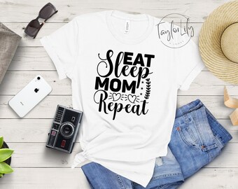 May include: White t-shirt with black text that reads "Eat Sleep Mom Repeat" with a heart and leaf design.