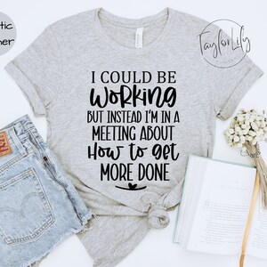 May include: A heather grey t-shirt with the text "I could be working but instead I'm in a meeting about how to get more done" printed in black.