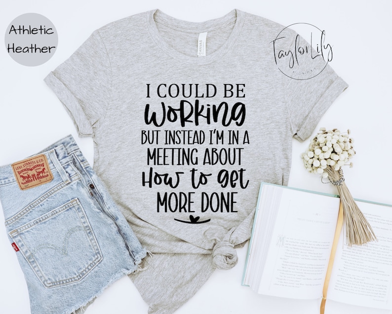 May include: A heather grey t-shirt with the text "I could be working but instead I'm in a meeting about how to get more done" printed in black.
