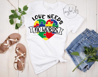Puede incluir: Camiseta blanca con un corazón de piezas de rompecabezas de colores y el texto "Love Needs No Words".
