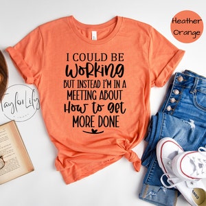 May include: A heather orange t-shirt with the text "I could be working but instead I'm in a meeting about how to get more done".