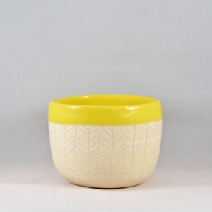 May include: A small white ceramic bowl with a yellow rim and a herringbone pattern.