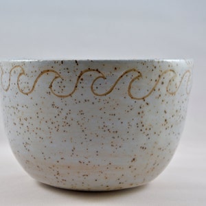 May include: A white ceramic bowl with a speckled glaze and a brown wavy design around the rim.