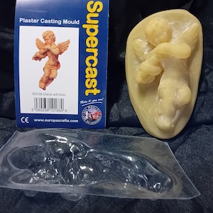 Puede incluir: Un molde de yeso para hacer una escultura de querubín. El molde está hecho de plástico transparente y muestra el diseño detallado del querubín sosteniendo un violín. El embalaje incluye el texto "Supercast" y "Molde de yeso".