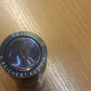 May include: Close-up of a silver bottle stopper with the text "PK 12,5+ C. REICHERT AUSTRIA" engraved around the rim.