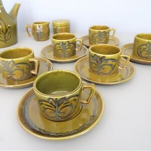 May include: A vintage olive green ceramic tea set with a leaf design. The set includes a teapot, creamer, sugar bowl, and several cups and saucers. The cups and saucers have a decorative pattern in a darker green and gold.
