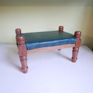 May include: A small wooden footstool with turned legs and a dark green leather top. The top is studded with metal tacks.