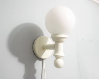 May include: White wall-mounted light fixture with a round, frosted glass shade and a white cord.