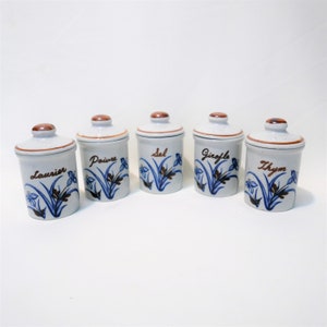 May include: Set of five white ceramic spice jars with brown lids and blue and brown floral designs. The jars are labelled "Laurier", "Poivre", "Sel", "Gingembre", and "Thym".