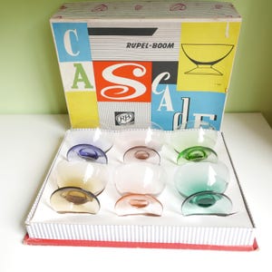 May include: A set of vintage Cascade dessert bowls in a box. The bowls are clear with colored bases in shades of blue, pink, green, and amber. The box has a colorful design with the word "Cascade" and "Rupel-Boom" printed on it.
