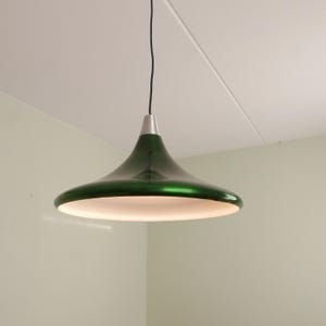 May include: A modern, green pendant light fixture with a flared shade and a silver-colored top. The light hangs from a black cord and illuminates the room below. The shade is approximately 20 inches in diameter.
