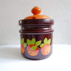 Op de afbeelding: Een bruine keramische pot met een deksel en een ontwerp van oranje en groene vruchten. De pot heeft een glanzende afwerking.