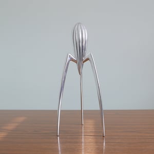 May include: A silver citrus juicer with a ribbed, cone-shaped top, standing on three legs.