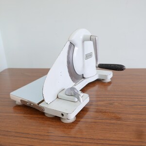 May include: White manual food slicer with a silver blade and a black handle. The slicer has a blue cutting board and the word "ROTIVA" is printed on the side.