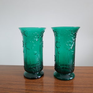May include: Two teal green glass vases with a floral design. The vases have a textured surface and a flared base.
