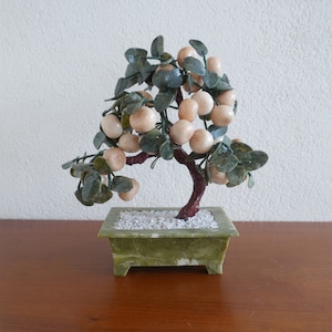 May include: A jade bonsai tree with green leaves and white jade fruit. The tree is potted in a green jade pot.